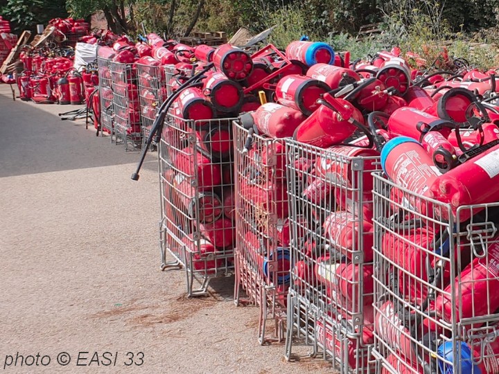 Vieux extincteurs � recycler en partance dans des conteneurs grillag�s.